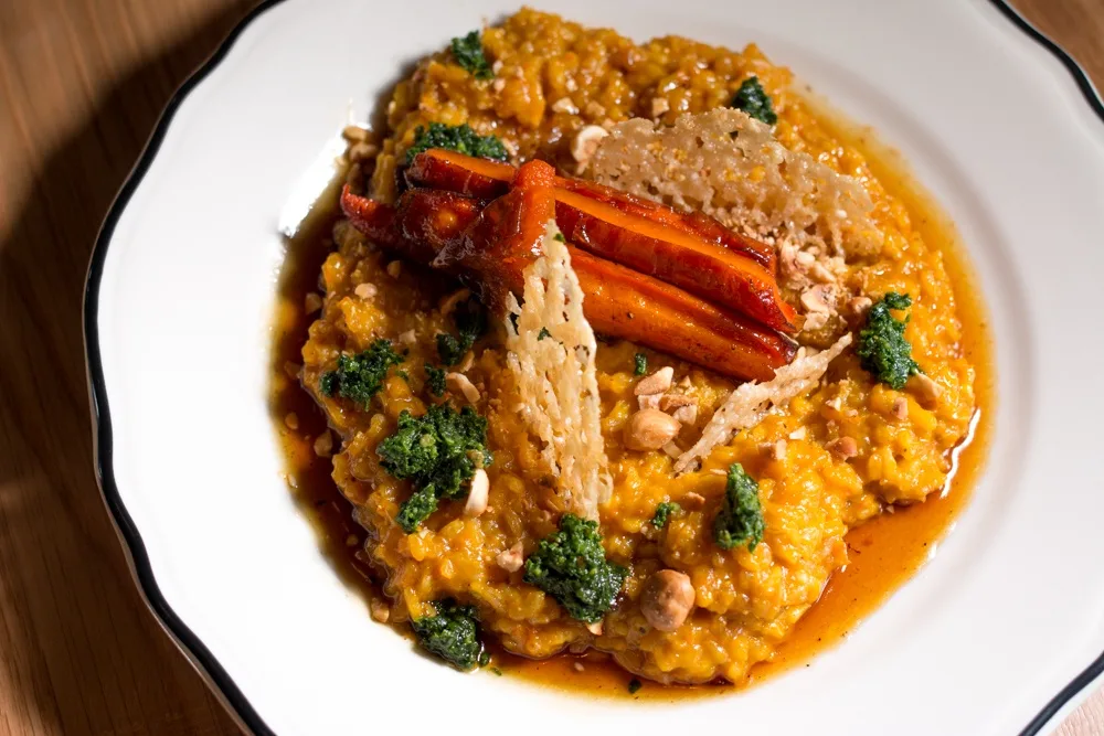 Roasted Carrot Risotto is prepared with Carolina gold rice, kale pesto, parmesan crisps and hazelnuts. The popular vegetarian dish uses carrots to excellent effect, coloring the rice with its bright orange hue.