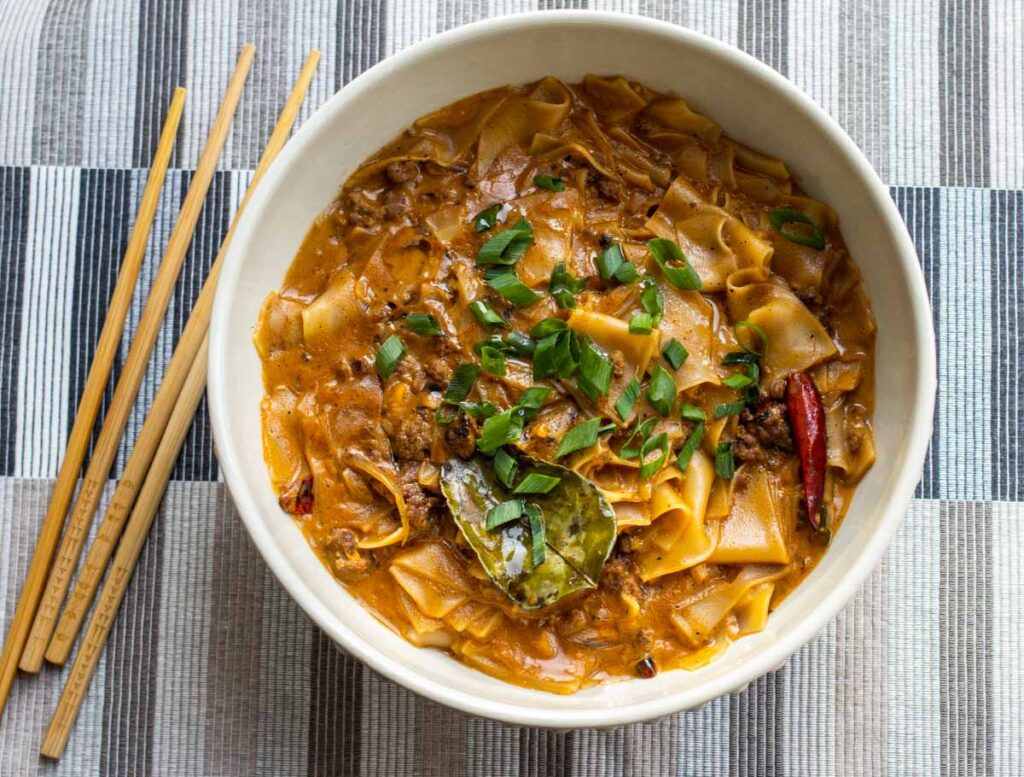 Thai Panang Curry Noodles with Meat Sauce on Striped Placemat and Chopsticks