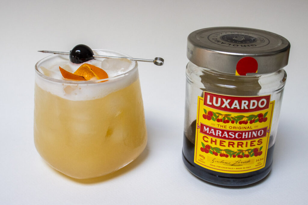 Whiskey Sour Next to Luxardo Cherries Jar