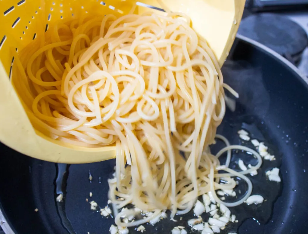 Dropping cooked pasta into a frying pan