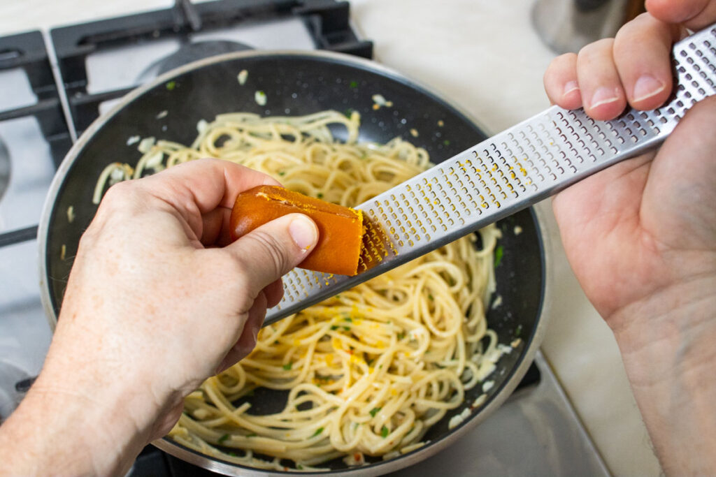 Grating Bottarga onto spaghetti in a frying pan
