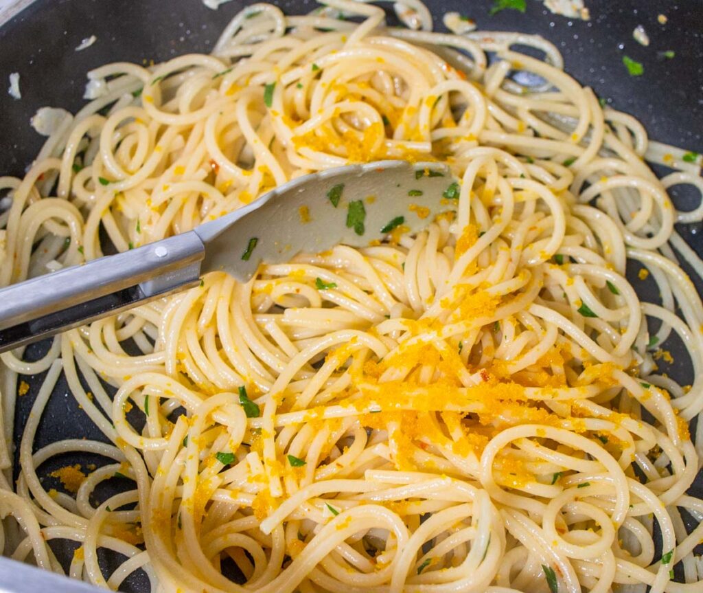 Mixing Spaghetti alla Bottarga in a frying pan with tongs
