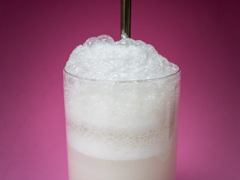 Ramos Gin Fizz Cocktail Up Close with Straw and Pink Background