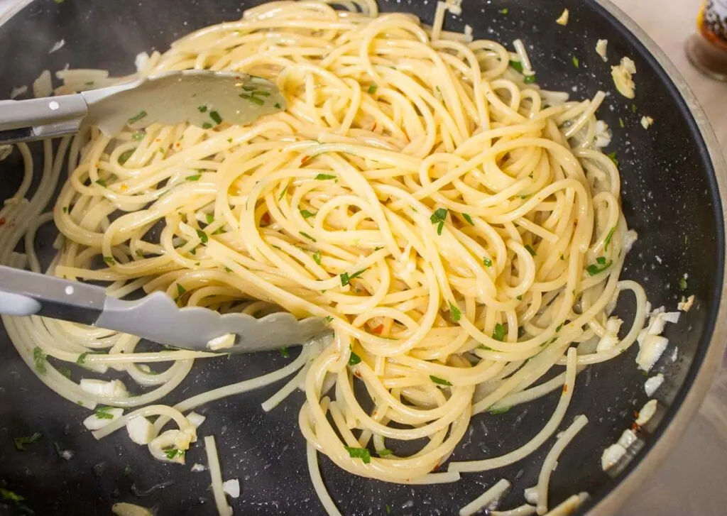 Stirring spaghetti with oil and garlic in a pan
