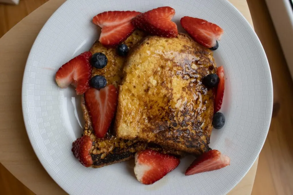 Oversoaked french toast on a plate with strawberries and blueberries