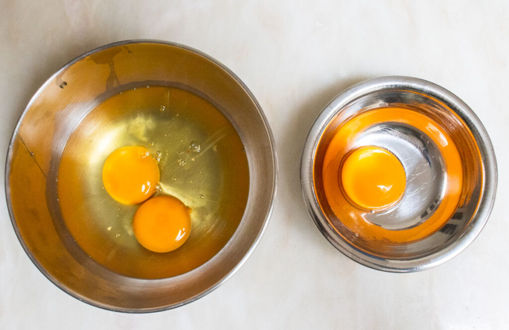 Two whole eggs and one whole egg yolk in silver bowls