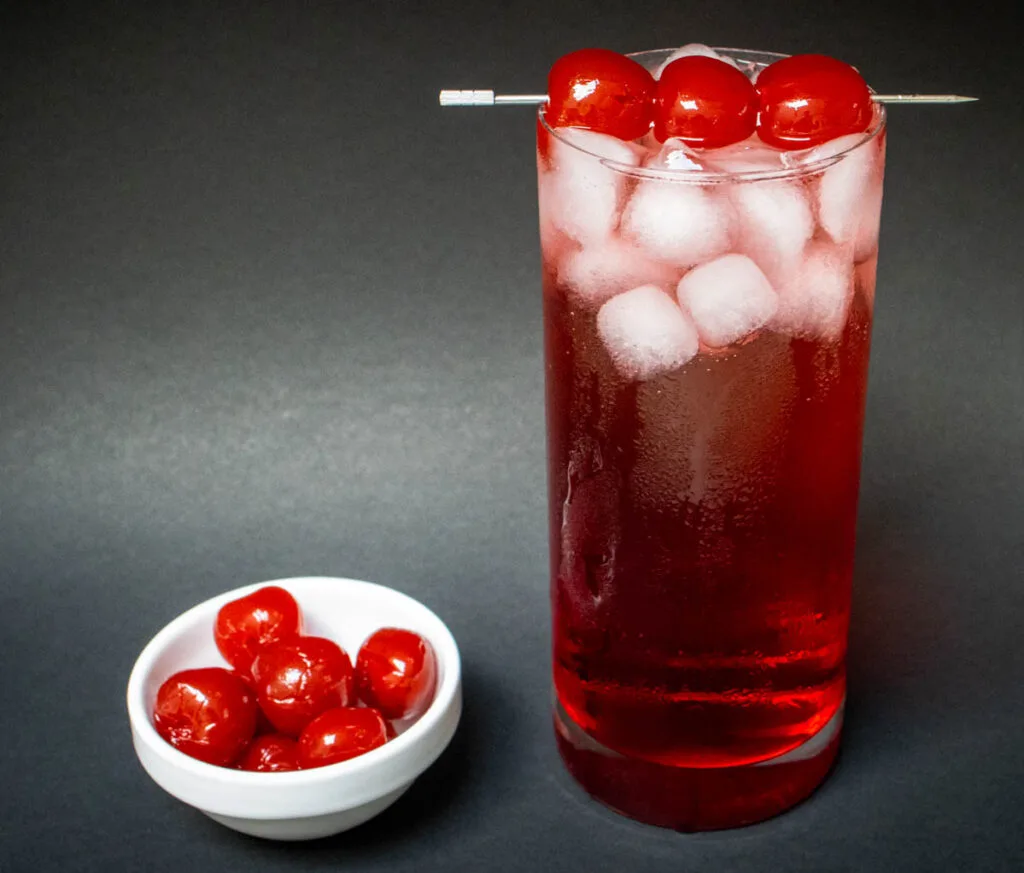 Dirty Shirley Cocktail with Black Background and Bowl of Cherries