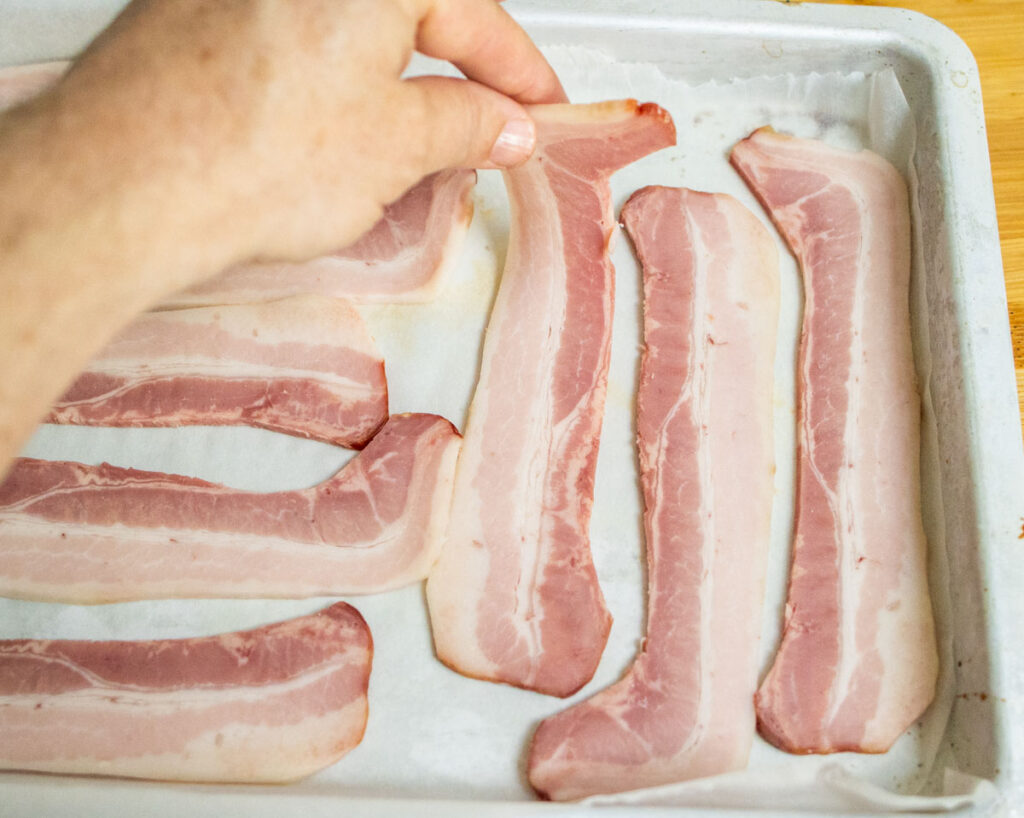 Placing raw bacon on a parchment lined baking sheet
