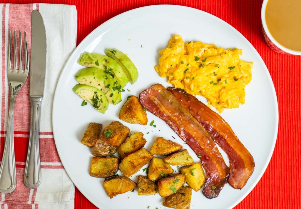 Potatoes, Avocado,Eggs and Maple Bacon on a White Plate with a Red Placemat