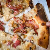 Pulling a slice of White Clam Pizza w Bacon at Frank Pepes in New Haven