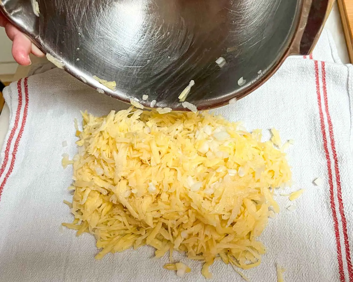 Grated potatoes and chopped onions being placed in a kitchen towel before wringing