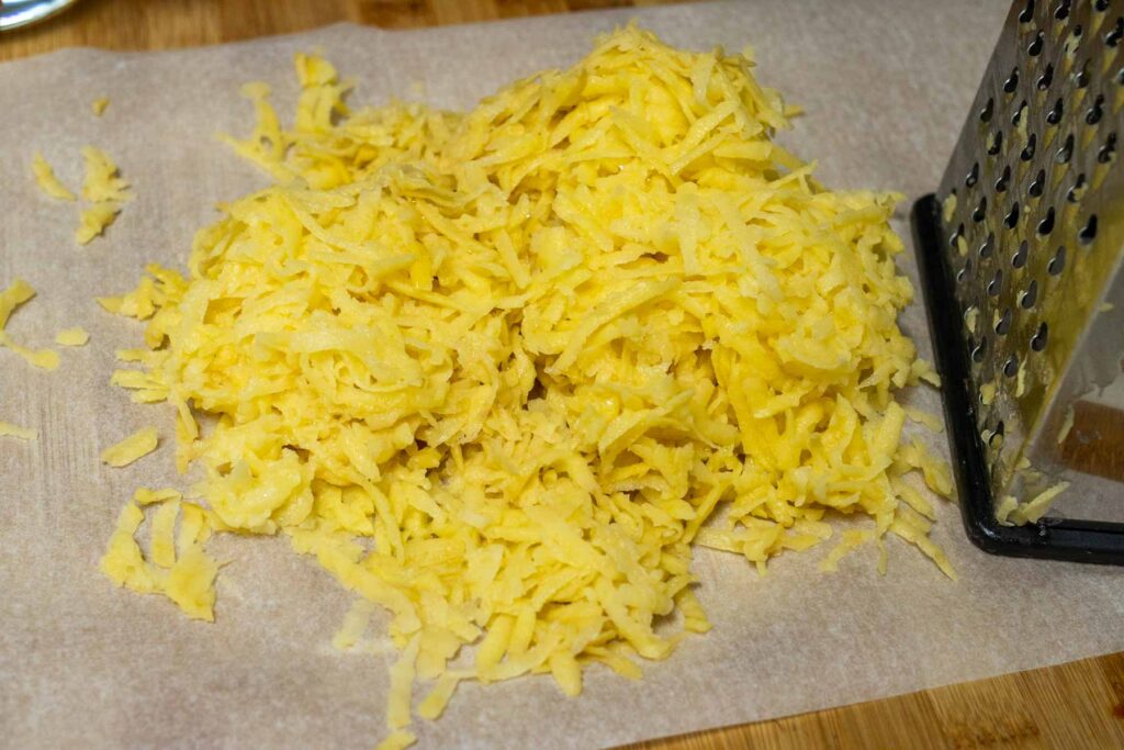 Grated potatoes on a sheet of wax paper in front of a box grater