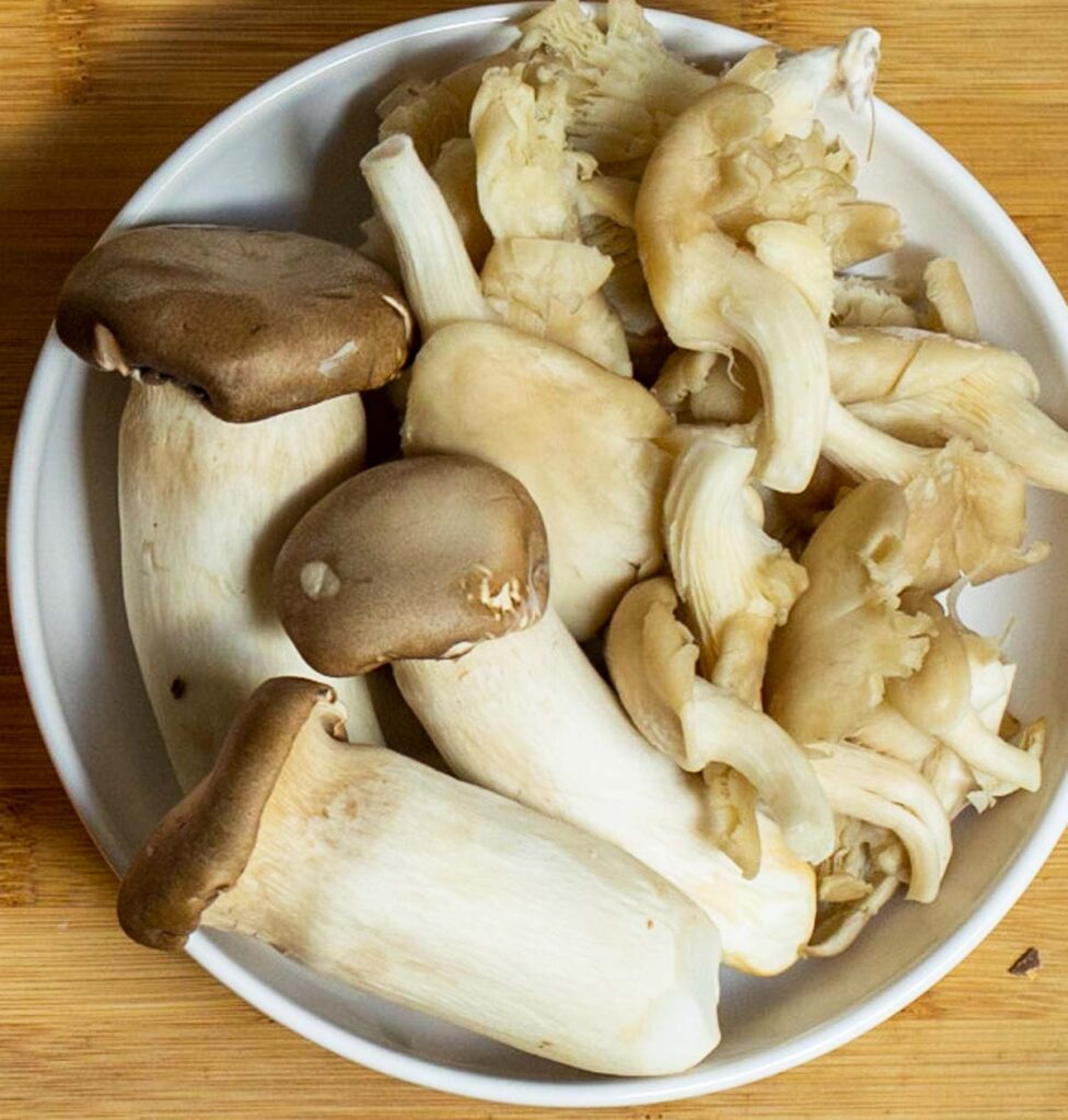 Raw trumpet and oyster mushrooms in a wide white bowl