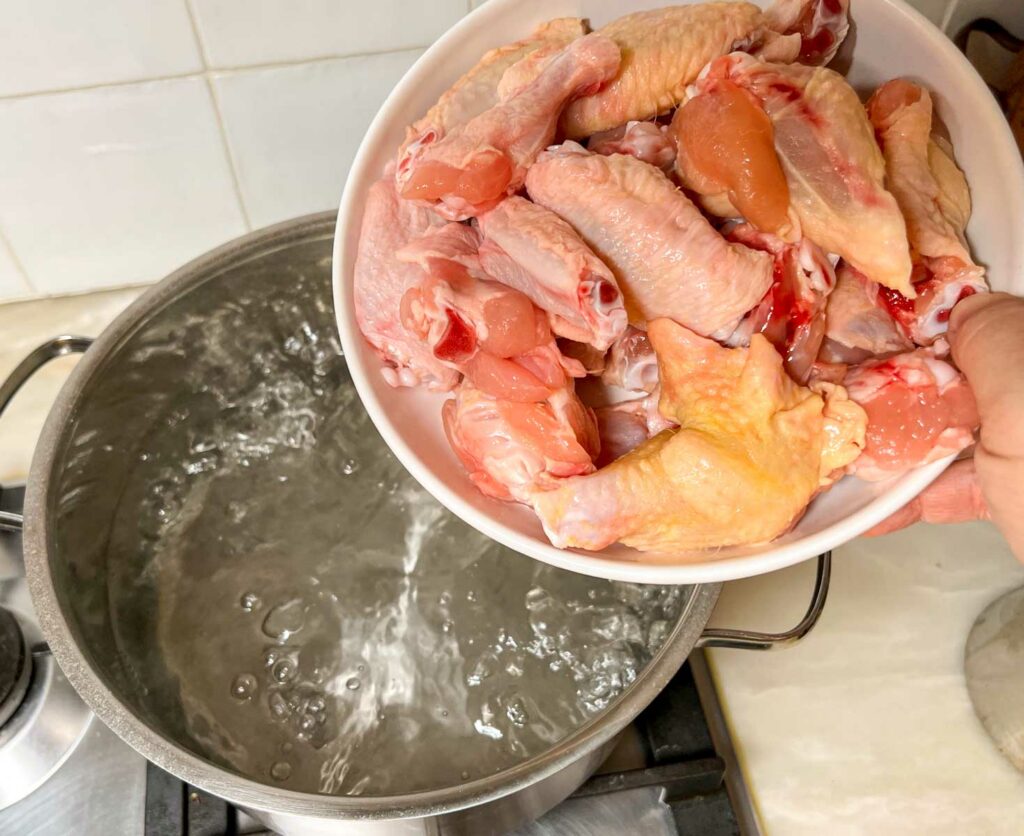 Placing raw chicken wings in a boiling water blanch