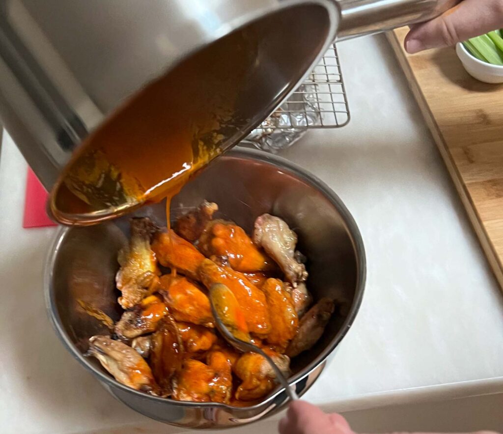 Pouring Buffalo wing sauce on wings