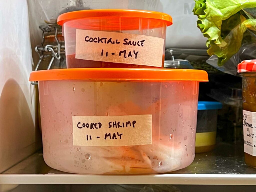 Containers of cooked shrimp and cocktail sauce in the refrigerator