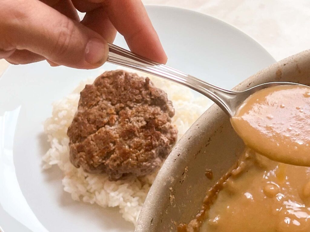 Spooning gravy on top of a burger and rice