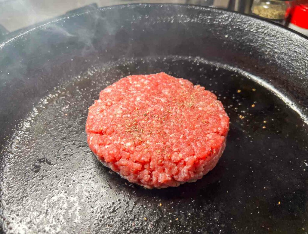 A hamburger cooking in a cast iron pan