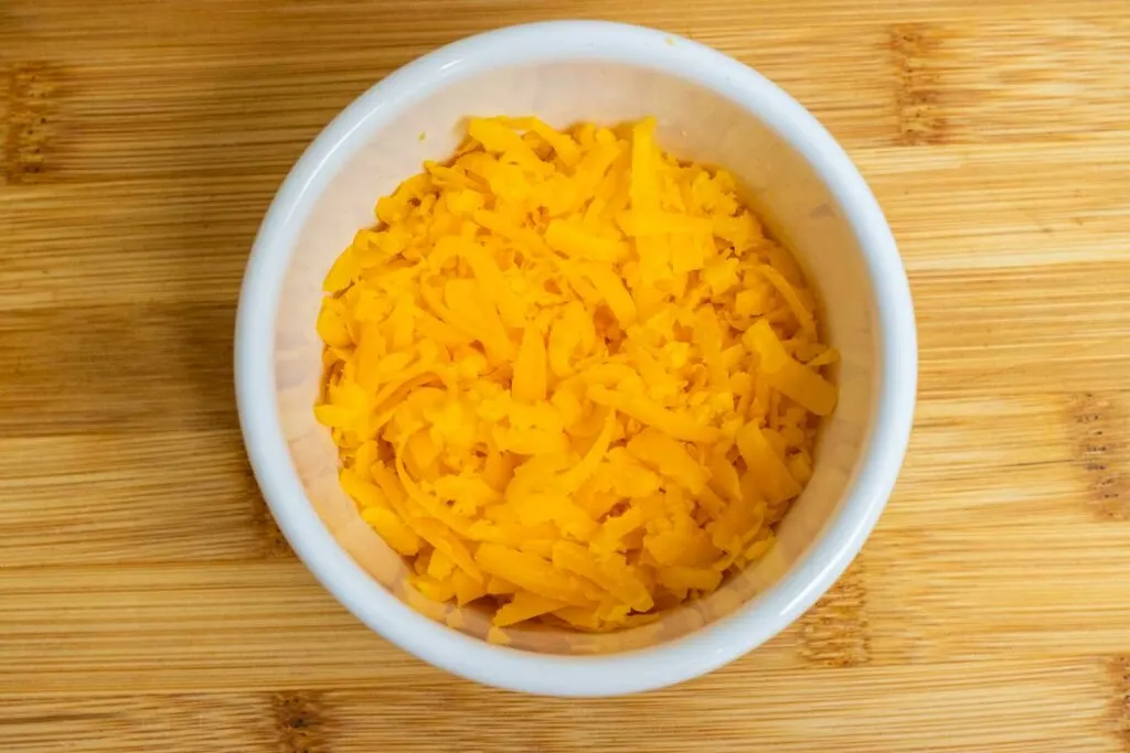 Grated Cheddar cheese in a white prep bowl