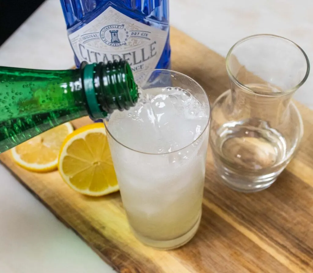 Pouring Seltzer into a Tom Collins Cocktail