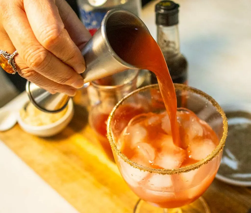 Pouring Clamato Juice into a Bloody Caesar Cocktail