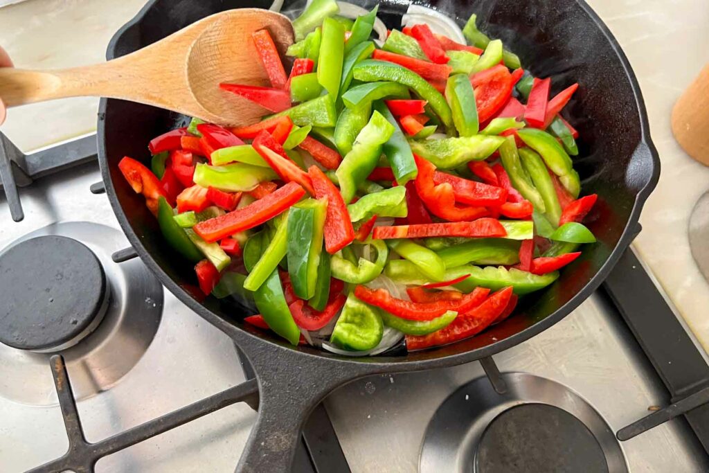 Stirring the Onoins and Peppers in a cast iron skillet